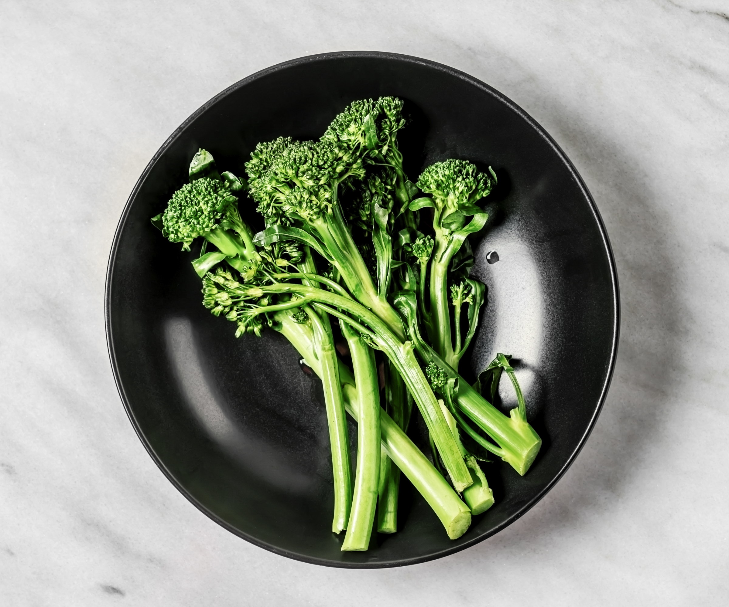 Steamed broccolini on a black plate against a white background