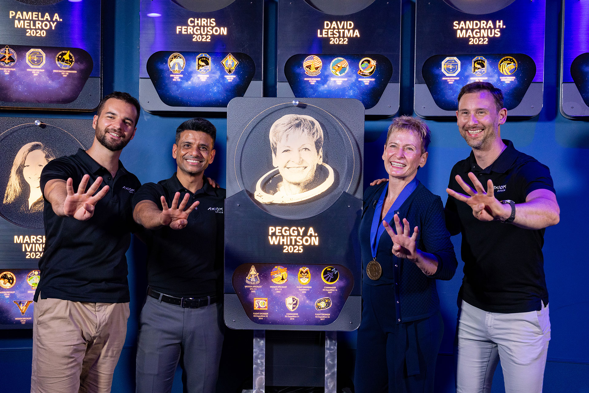 three men and woman pose with a plaque bearing the likeness of the woman while all four hold up four fingers
