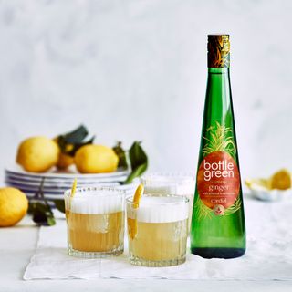 Bottle of ginger drink with two short glasses beside bottlegreen