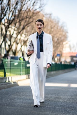 a guest at Milan Fashion Week wearing a white suit with a blue tie and black shirt