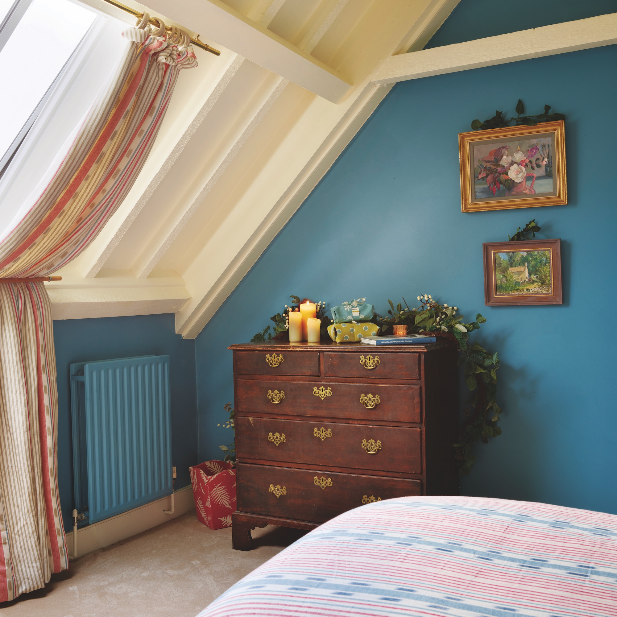 eaves bedroom with curtains held back by rail, wooden dresser and blue walls