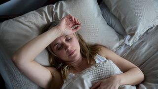 Middle-aged woman in bed with her right arm over her forehead looking like she is struggling to sleep