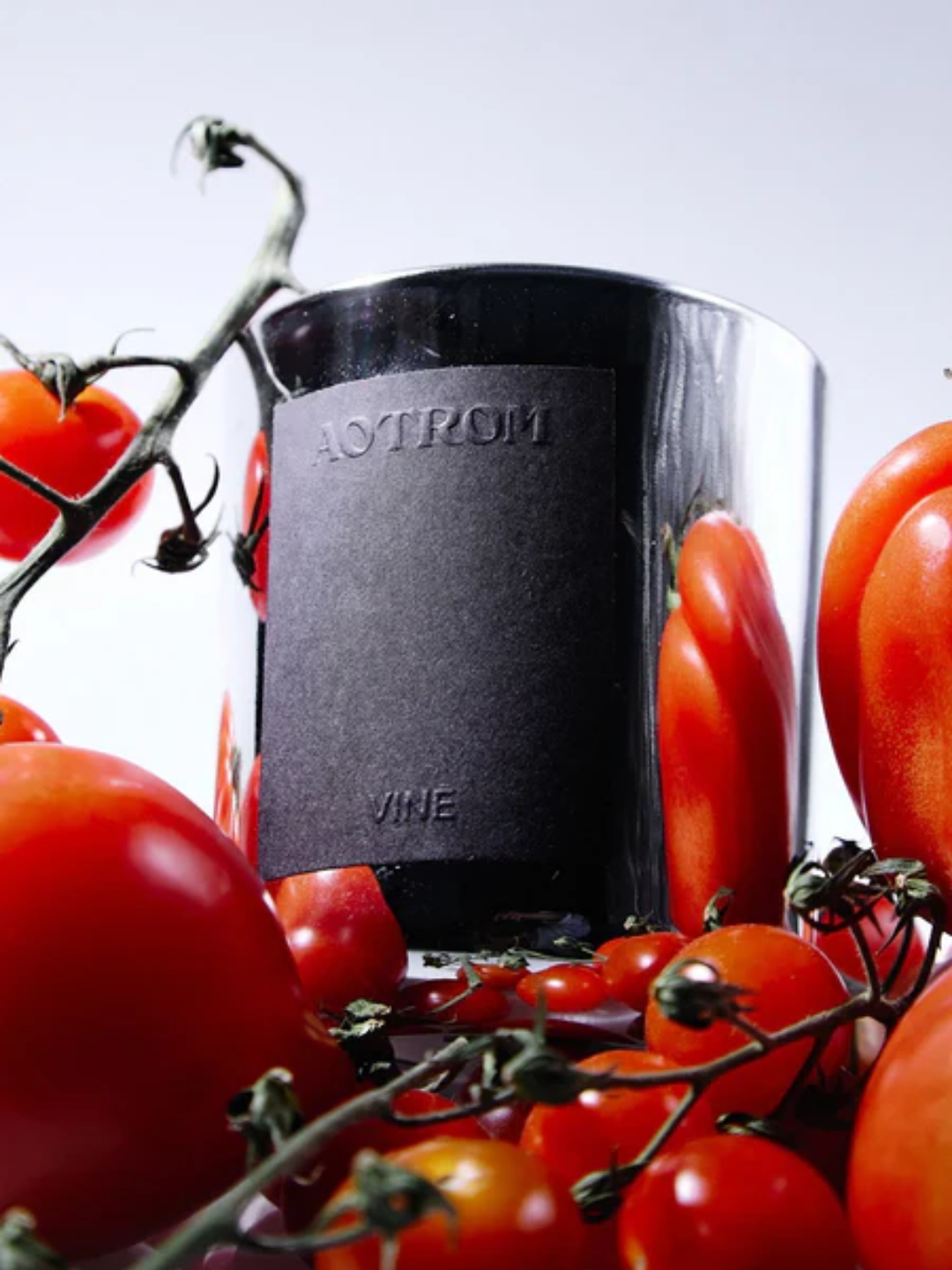 A chrome scented candle around tomatoes on vine