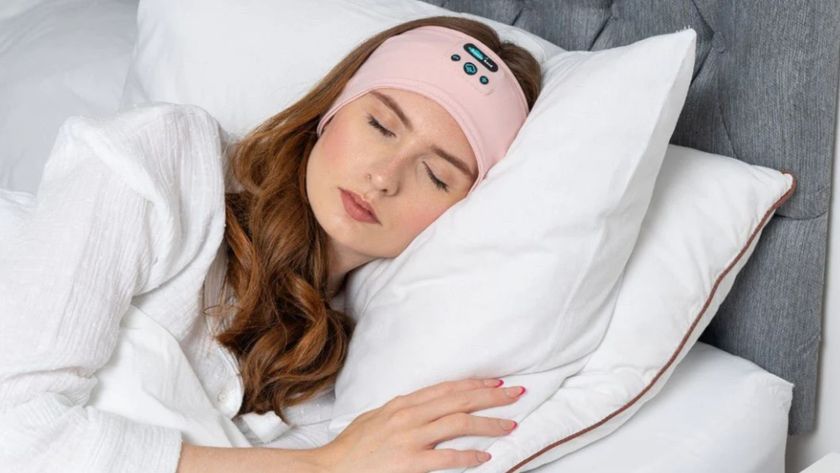 A woman with red hair wearing a pink sleep headband sleeping on her side in white bed and white pyjamas