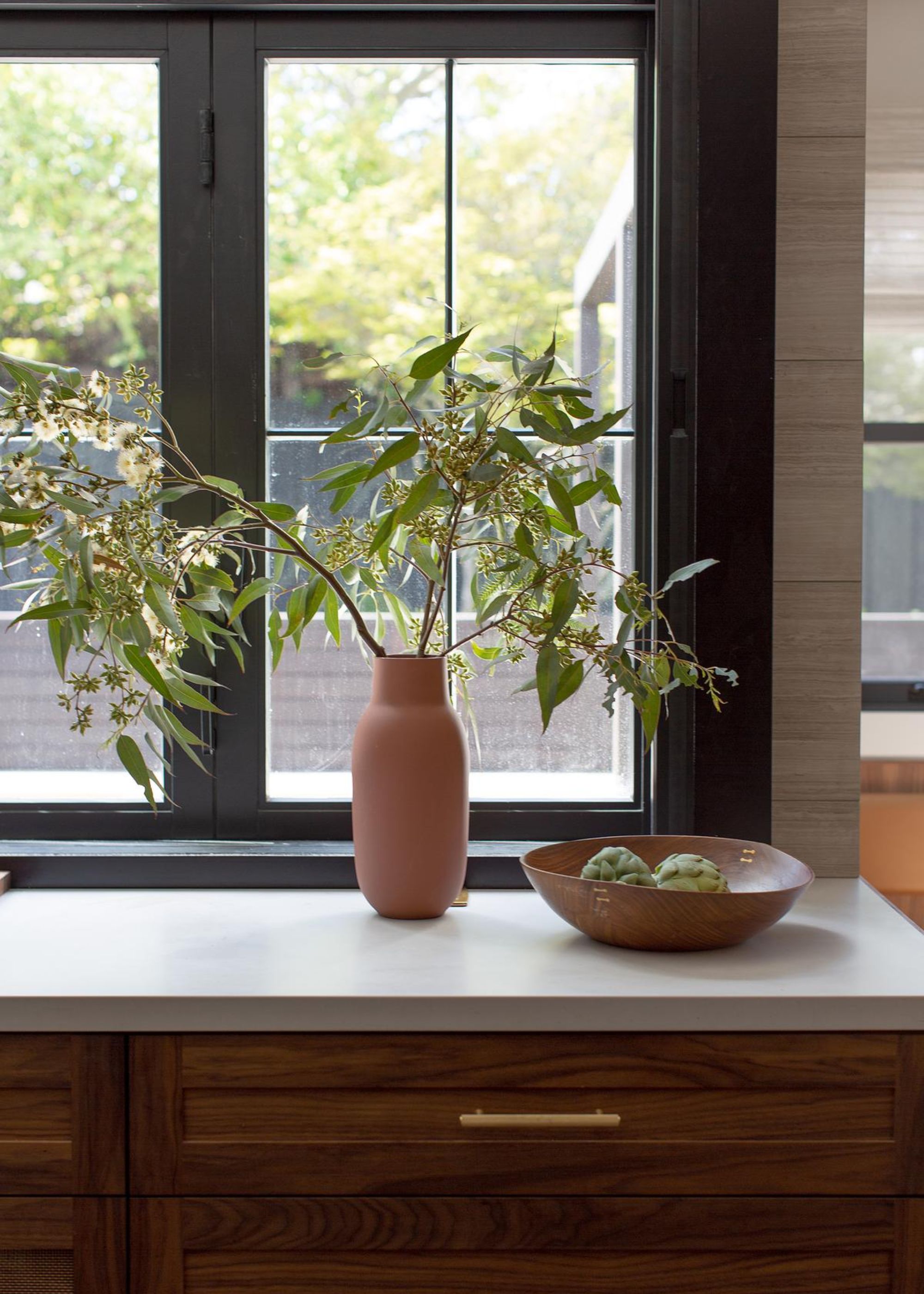 A view of a section of a kitchen countertop with a bowl on top as well as a vase with plants hanging out of it