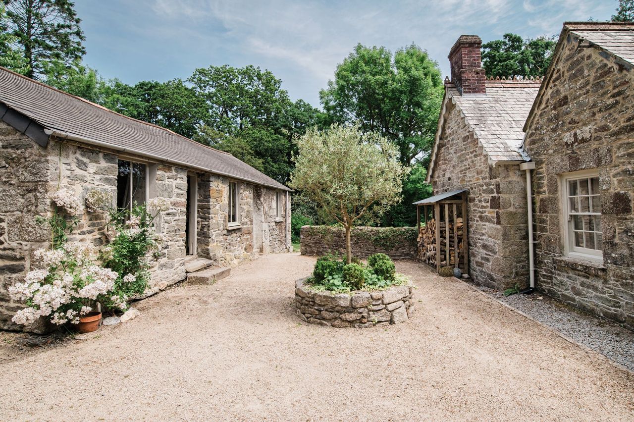 The back of the stone house shows a gravelled pathway with a stone barn behind the home as well