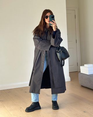 Woman wears trench coat, blue jeans and ankle boots