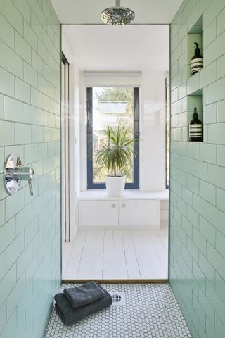 An en suite bathroom/shower room with mint green wall tiles and white floor tiles
