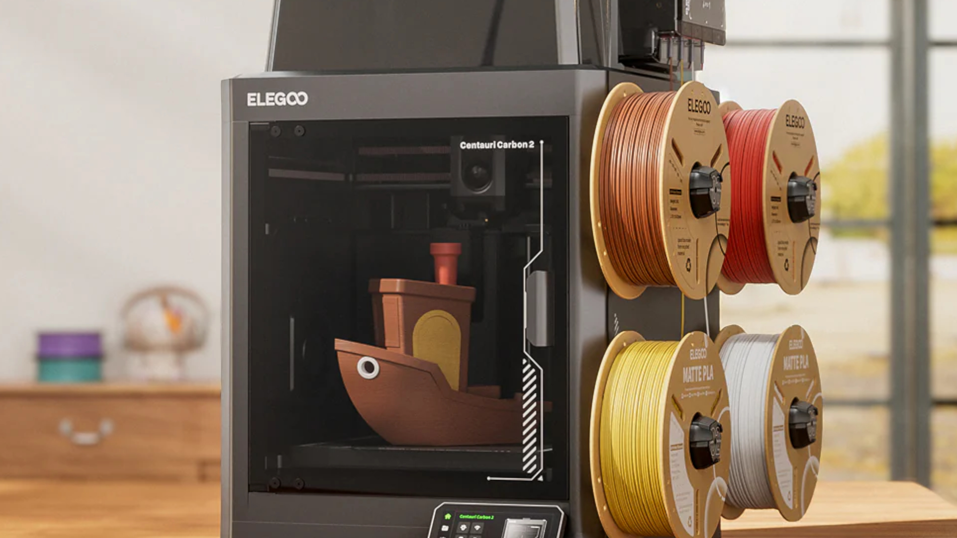 Elegoo Centauri Carbon 2 with filament reels on the side and a boat model inside, sat on a wooden surface in a home setting