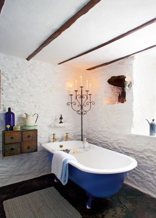 blue roll top bath with plaster walls and candle holder
