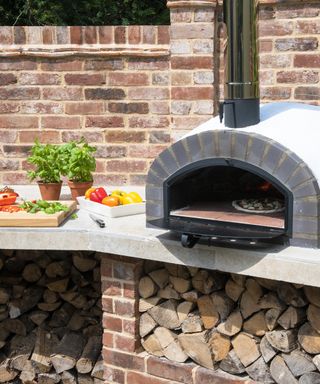 A pizza oven in an outdoor cooking area with pots of basil herbs