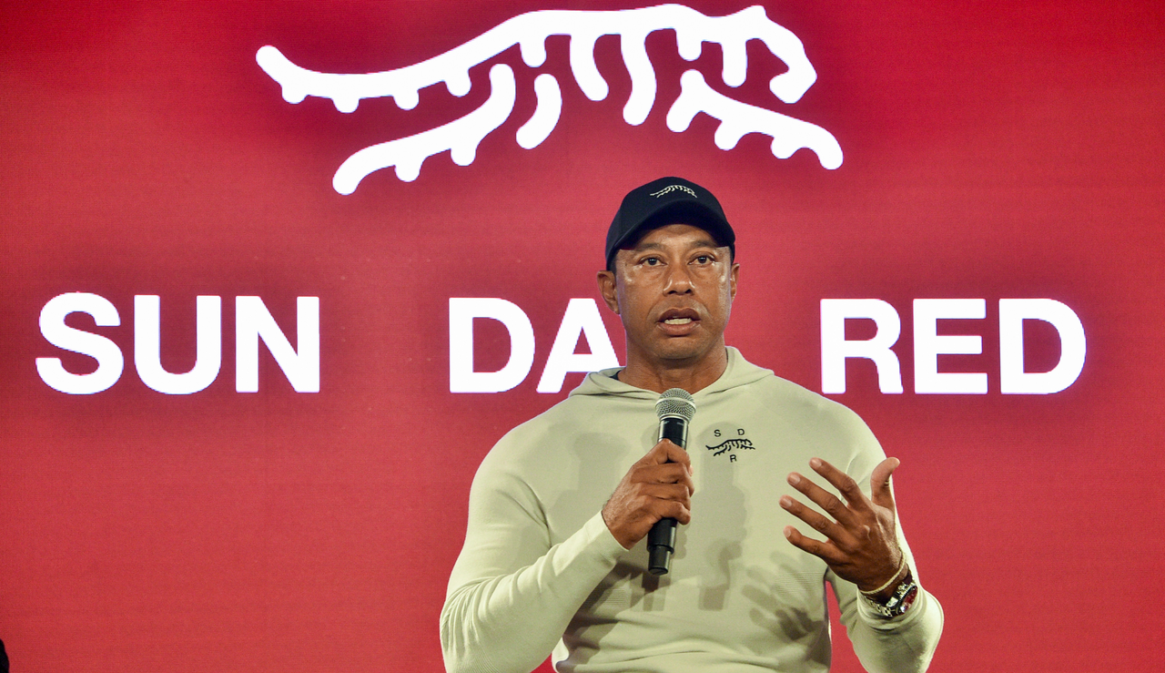Tiger Woods speaks in front of a Sun Day Red board