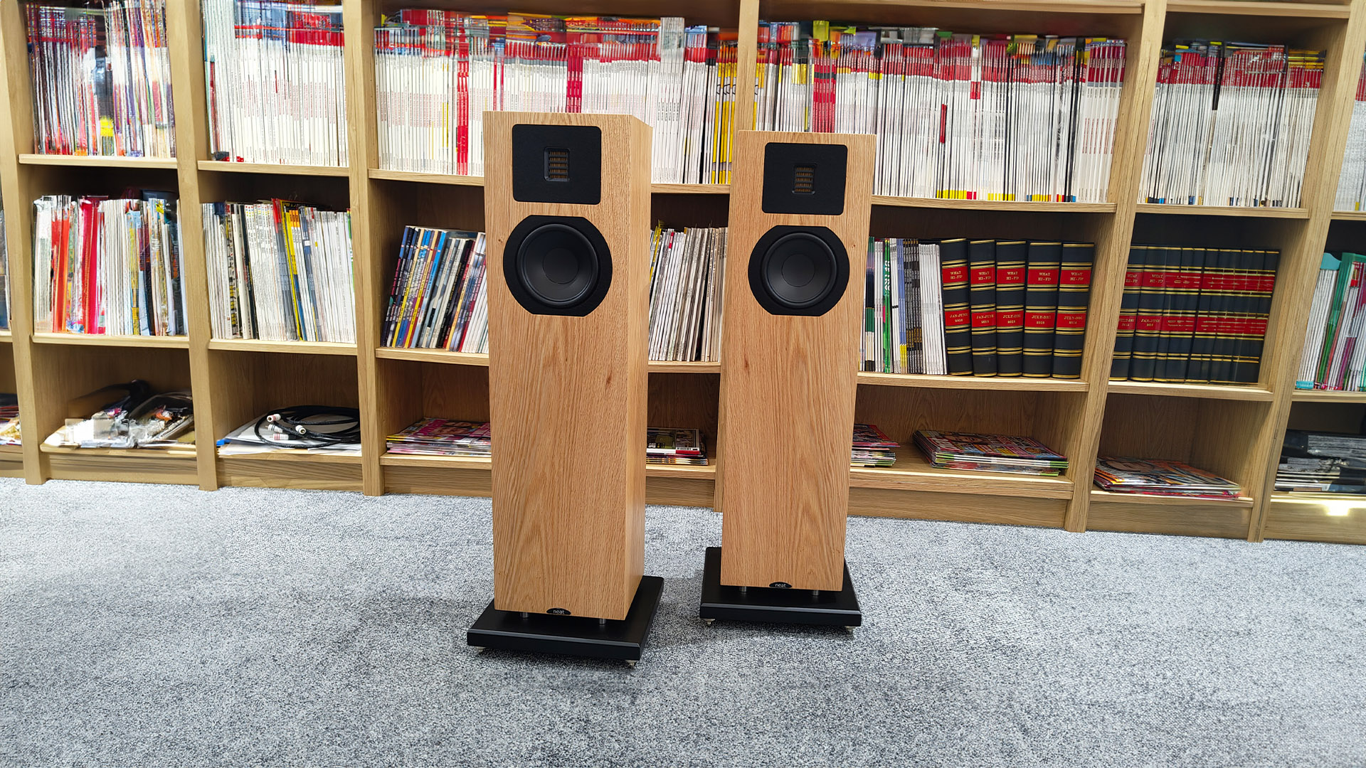 Neat Mystique Classic floorstanding speakers on grey carpet in front of bookcase