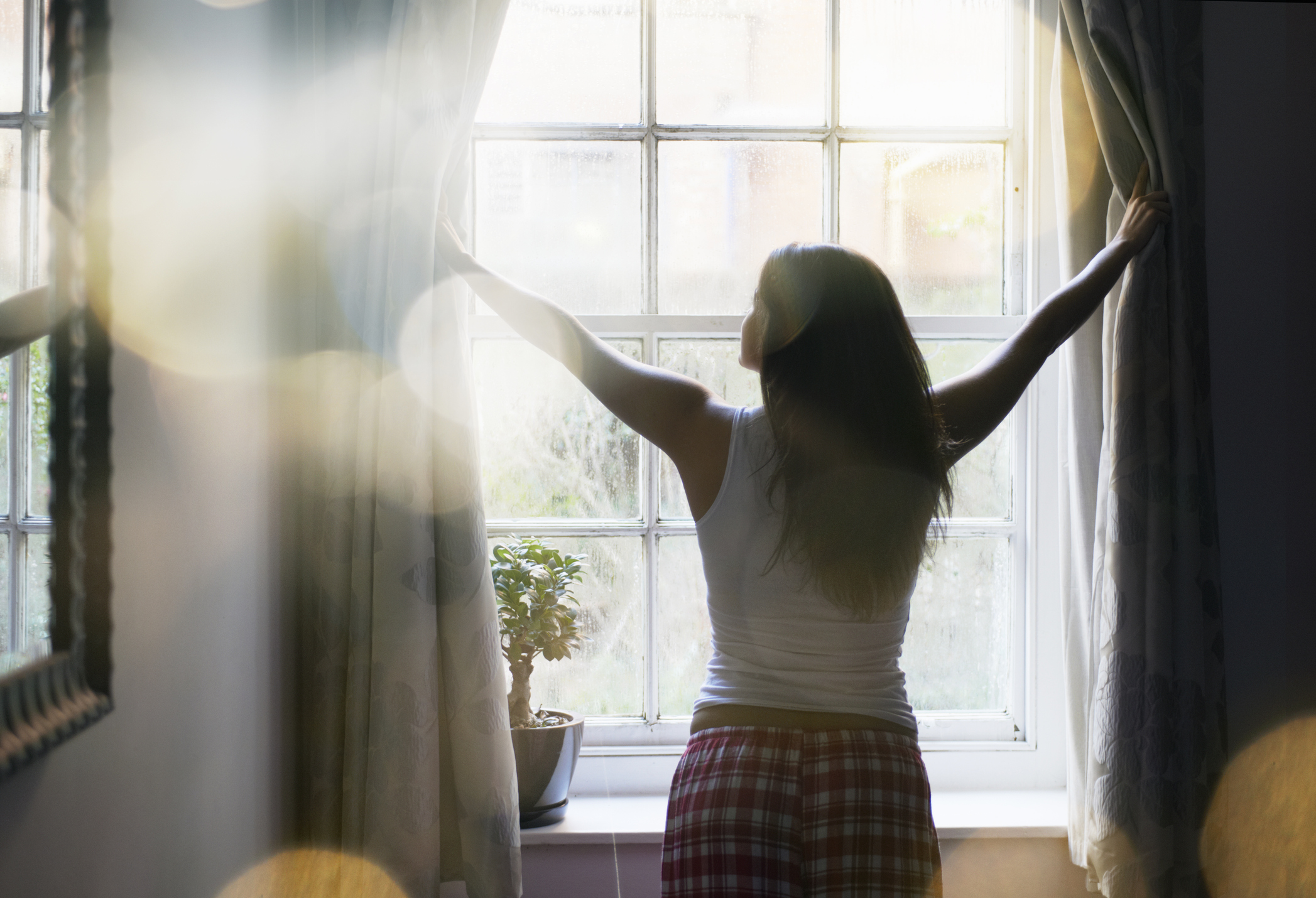 Eine Frau zieht morgens die Vorhänge zurück, um natürliches Sonnenlicht in ihr Schlafzimmer zu lassen