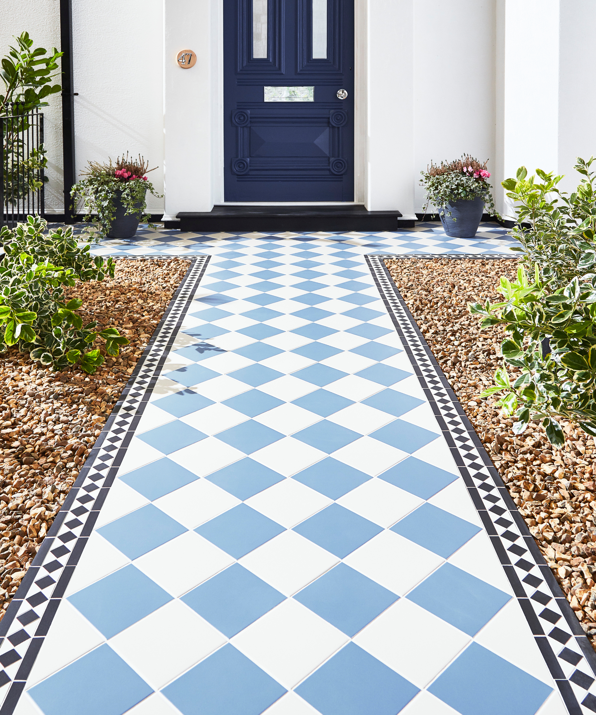 blue and white chequerboard tiled path leading to navy front door with small decorative border, gravel to side and plants
