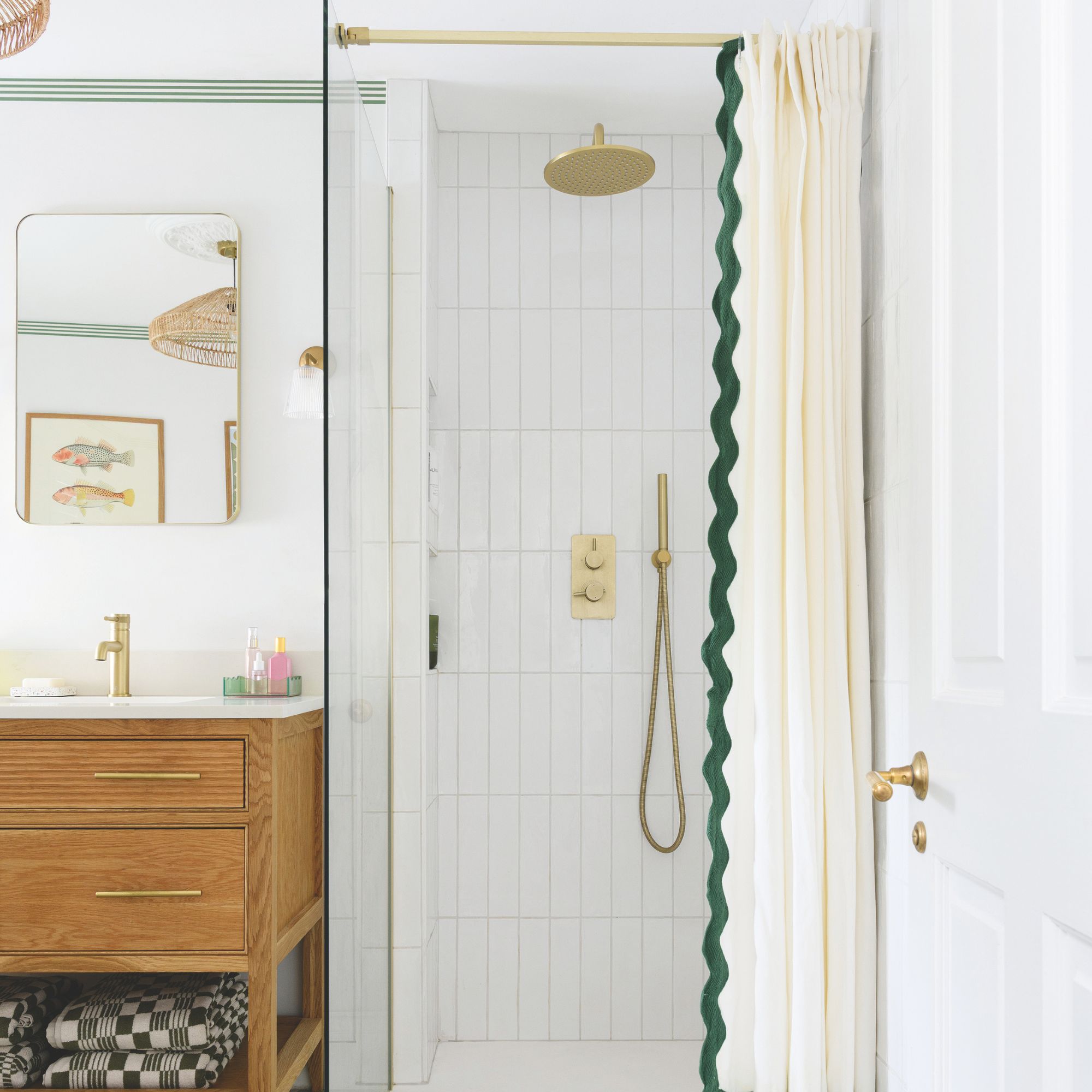 White tiled bathroom looking into a shower cubicle with gold hardware and a cream shower curtain with green wiggly trim