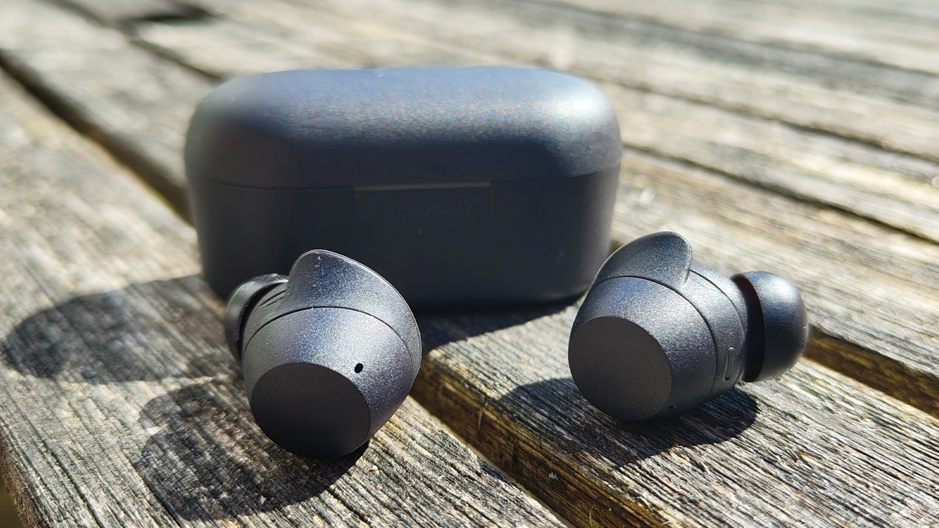 LG Xboom Buds 2025 wireless earbuds next to charging case on wooden table in sunshine