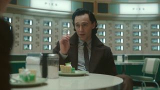 Tom Hiddleston gestures with a forkful of pie while telling a story in Loki Season 2, Episode 2.