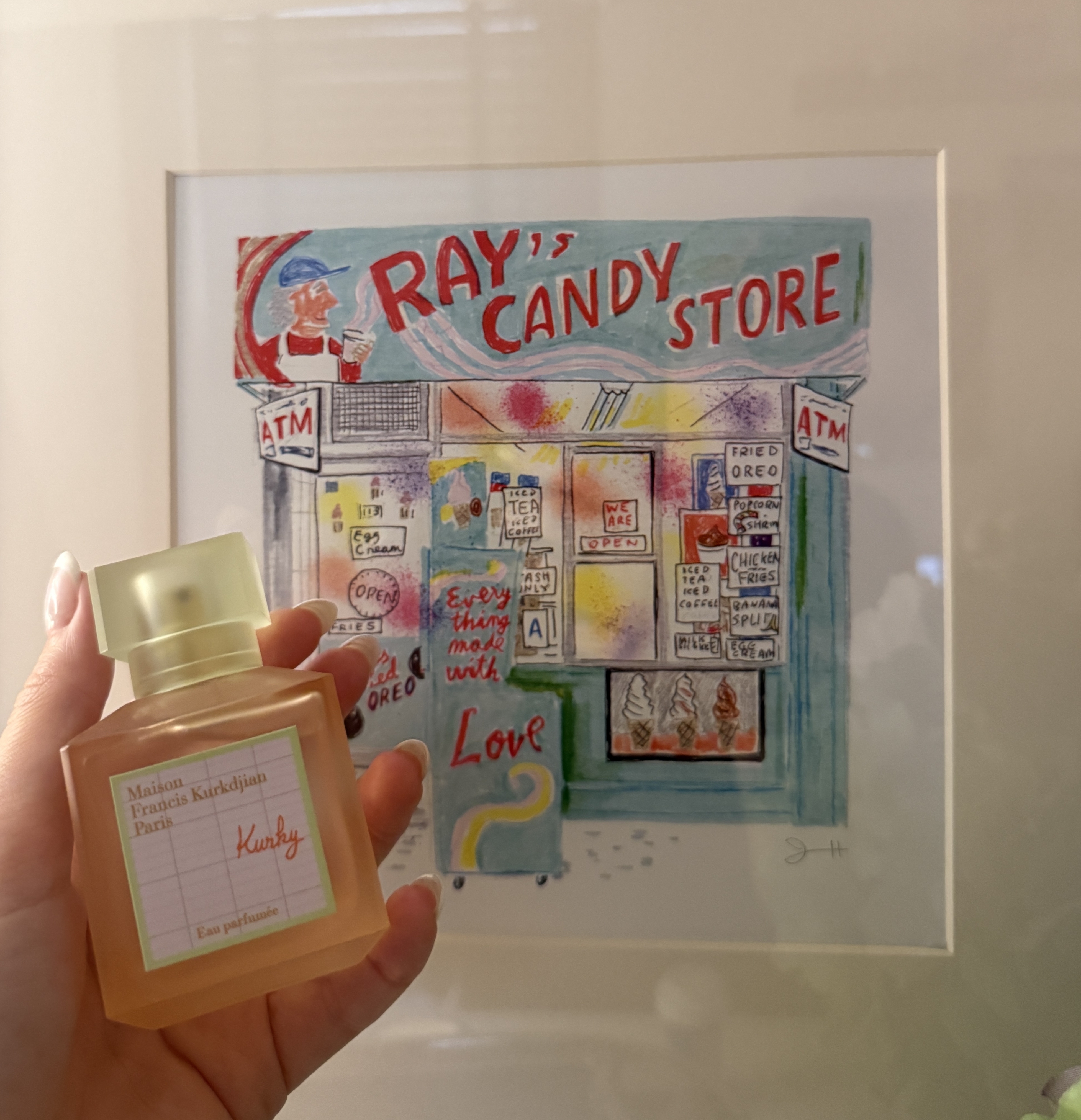 a girl holding up an orange and green perfume kurky in front of a painting of NYC ray's candy store that's colorful with blue and red candy