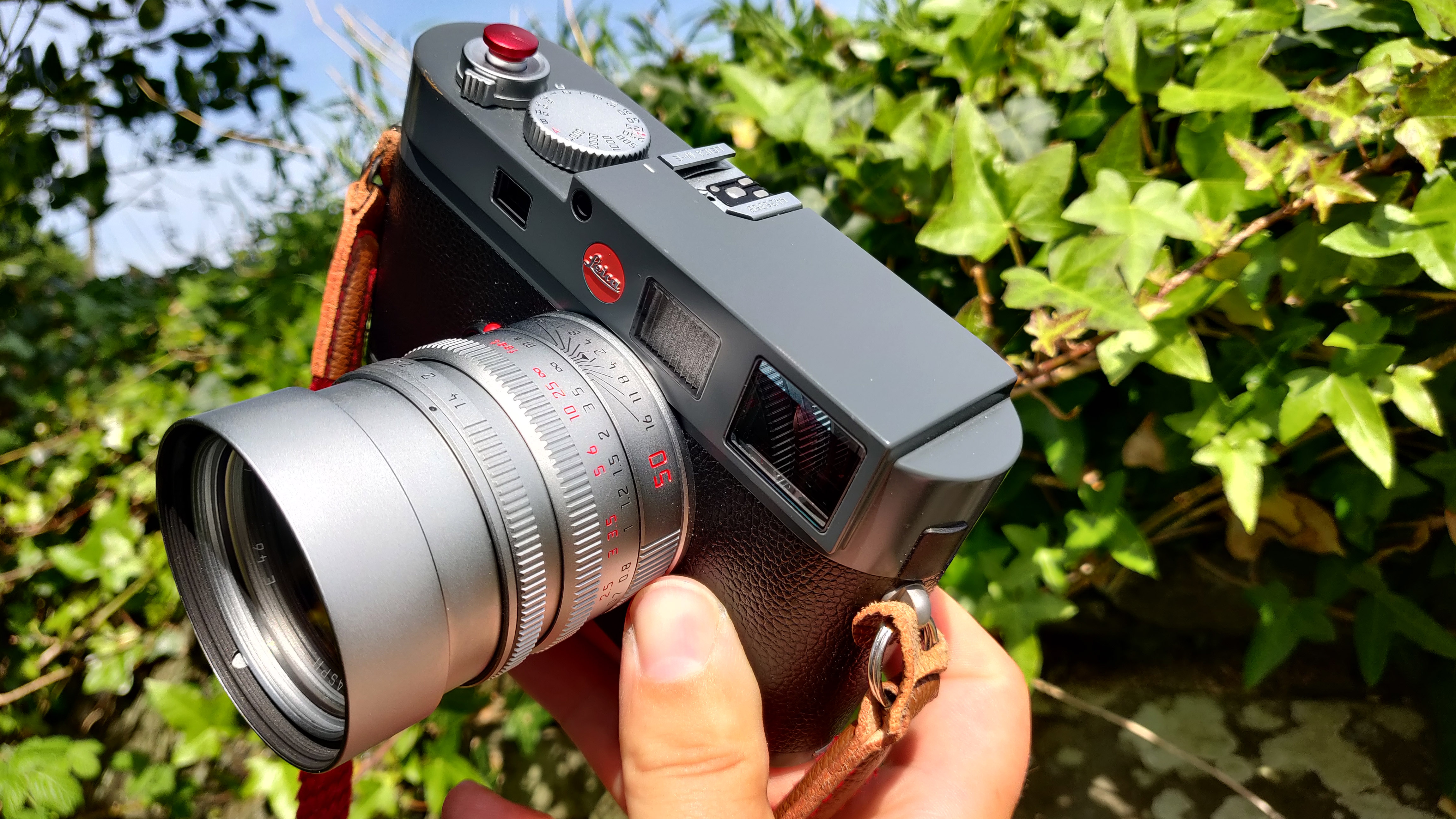 A Leica 50mm Summilux-M ASPH V1 attached to a camera, held by the hand up i the air