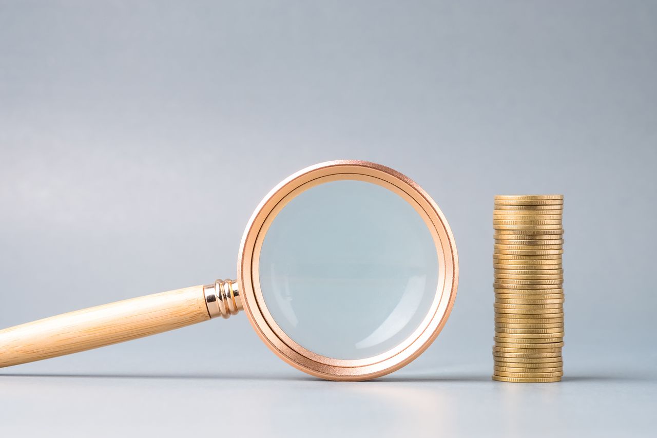 picture of gold magnifying glass next to a stack of gold coins