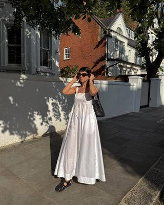 Woman on street wears white dress, fisherman sandals and woven bag