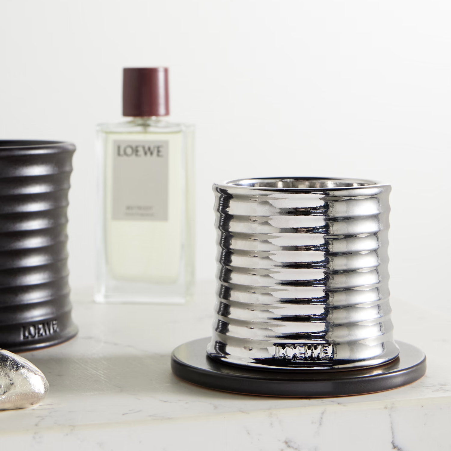 A chrome candle on a black coaster beside a room spray and a black candle
