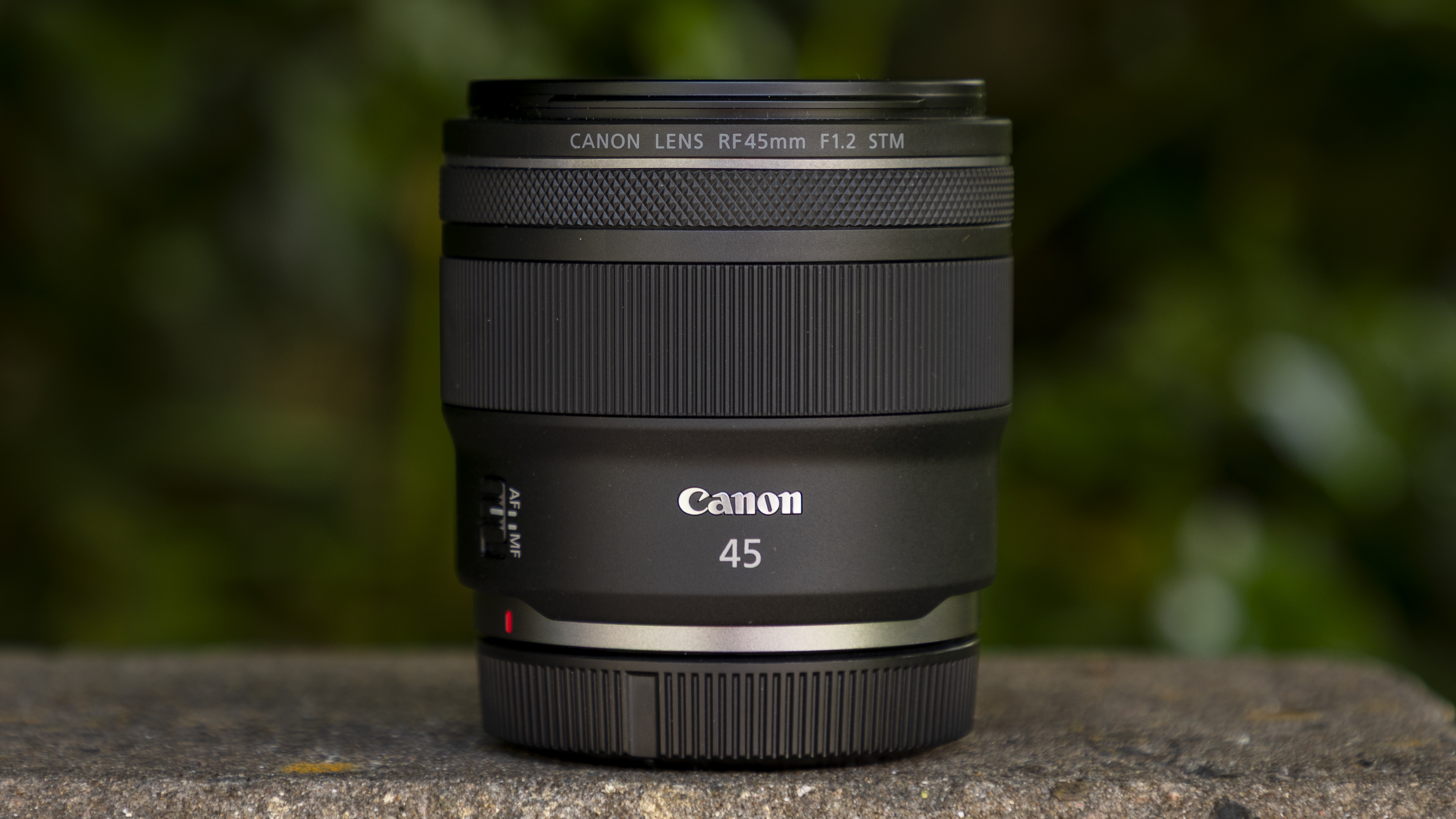 Canon RF 45mm F1.2 STM on a wall with greenery blur behind