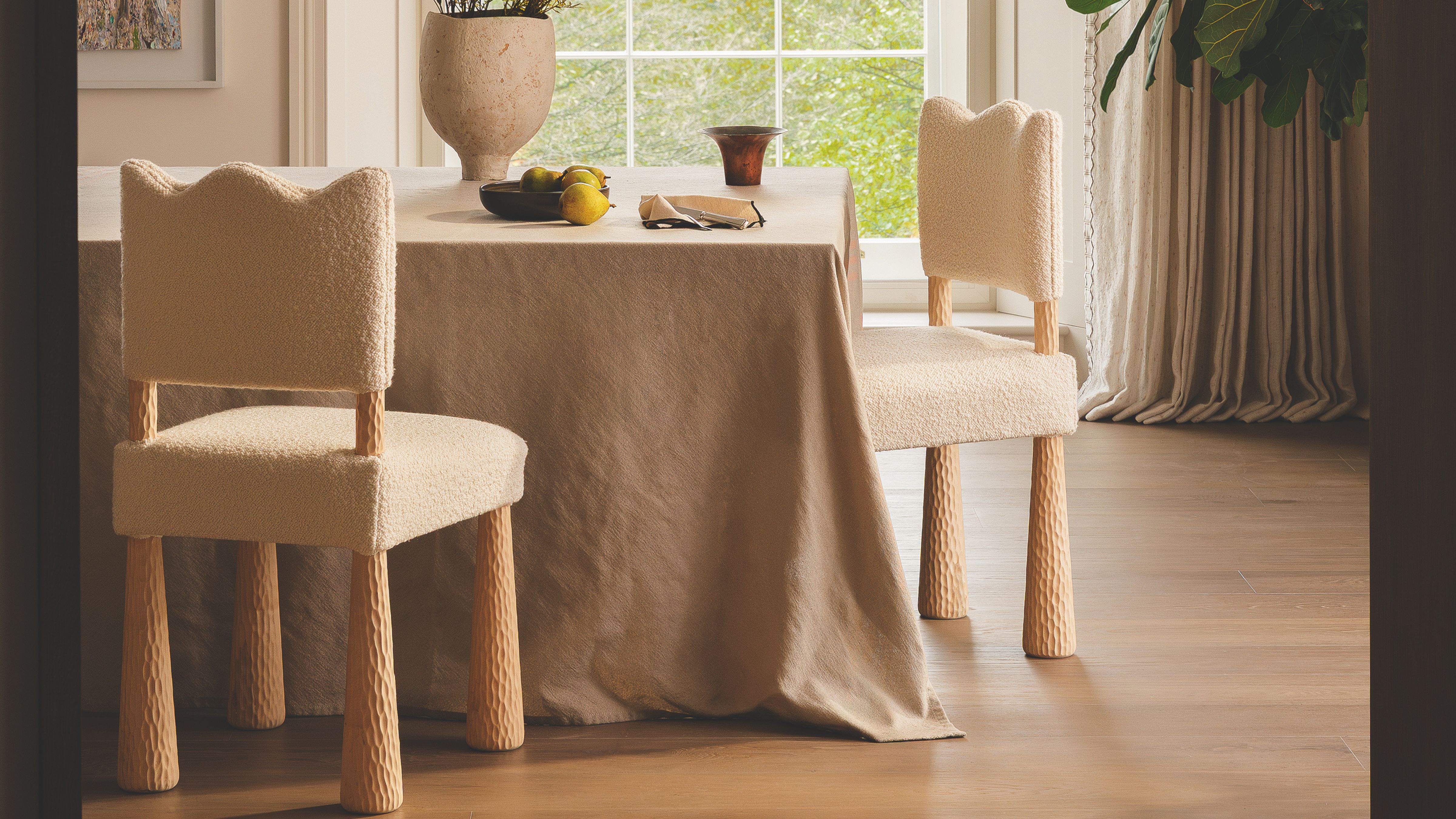 Neutral dining room area featuring wavy-bordered dining chairs and a linen tablecloth