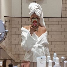 A woman in a white bathrobe taking a mirror selfie