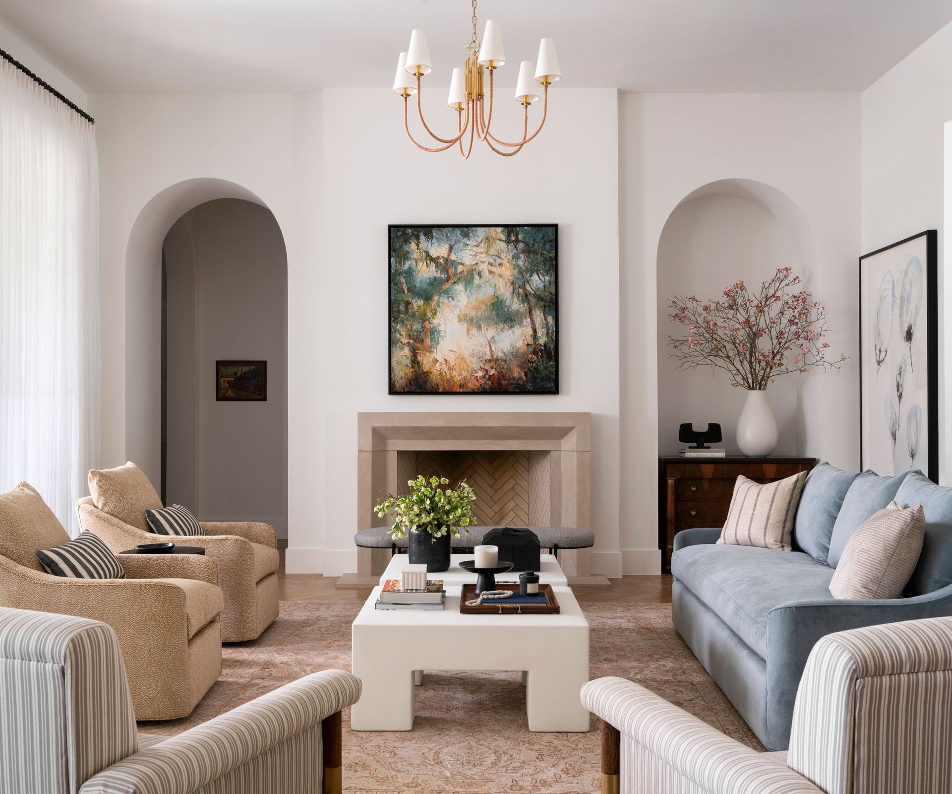 Neutral living room with arched doorways and blue sofa, striped armchairs and marble coffee table