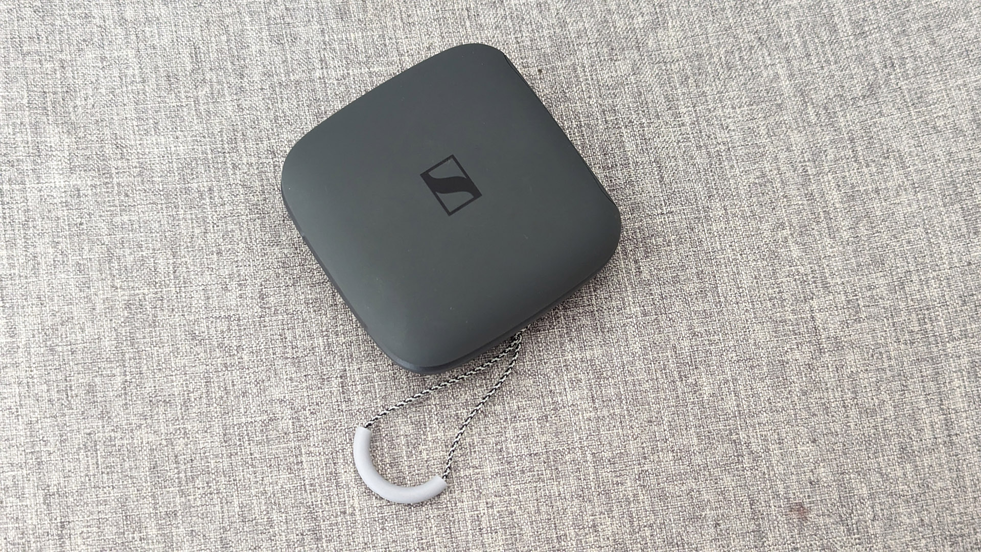 Sennheiser Momentum Sport in-ear headphones charging case on grey fabric background