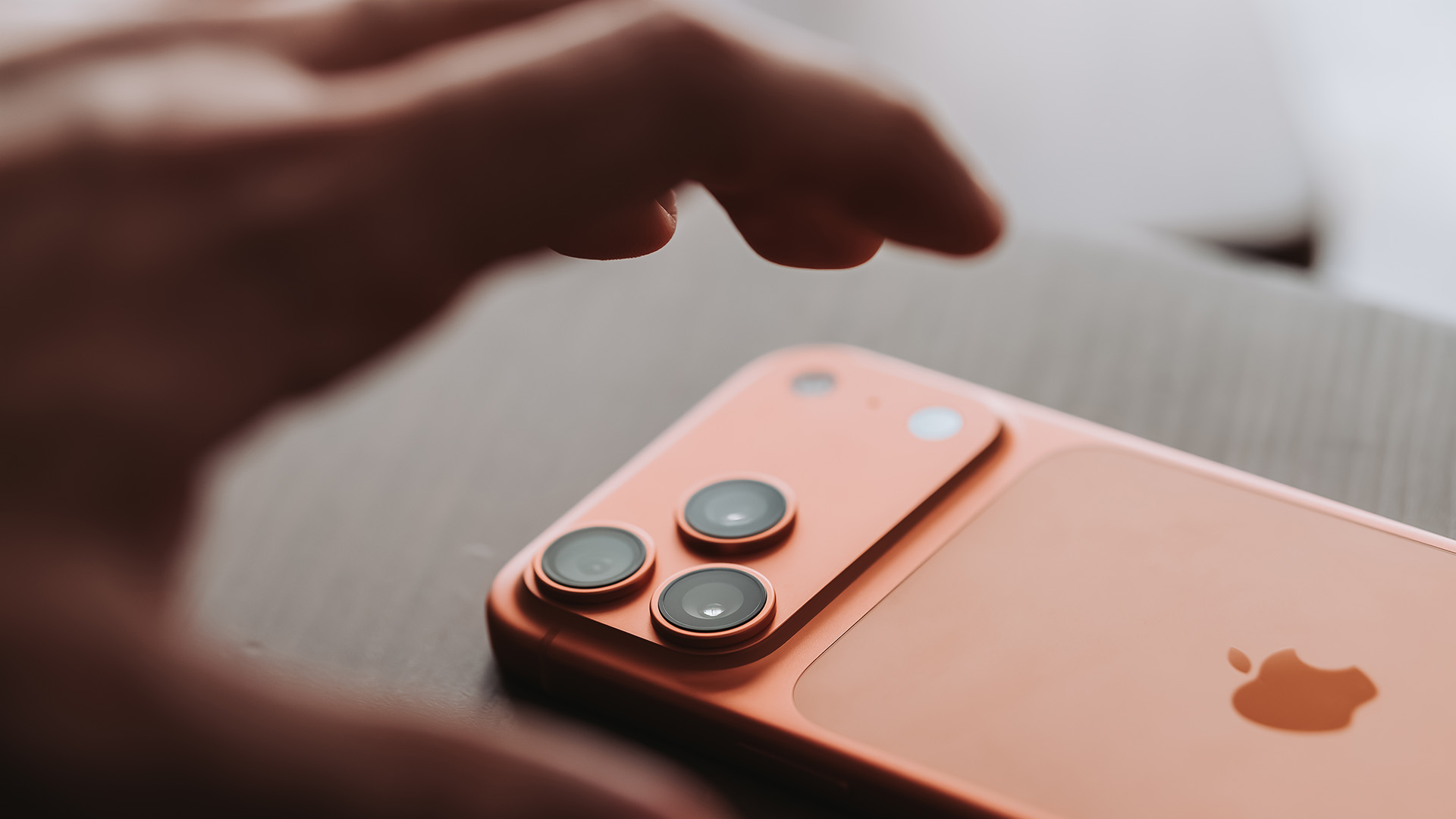 Apple iPhone 17 Pro lying on its front with a hand about to pick it up
