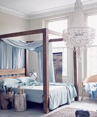 An example of bedroom chandelier ideas showing a bedroom with a netted fabric chandelier, four poster bed and blue bedding