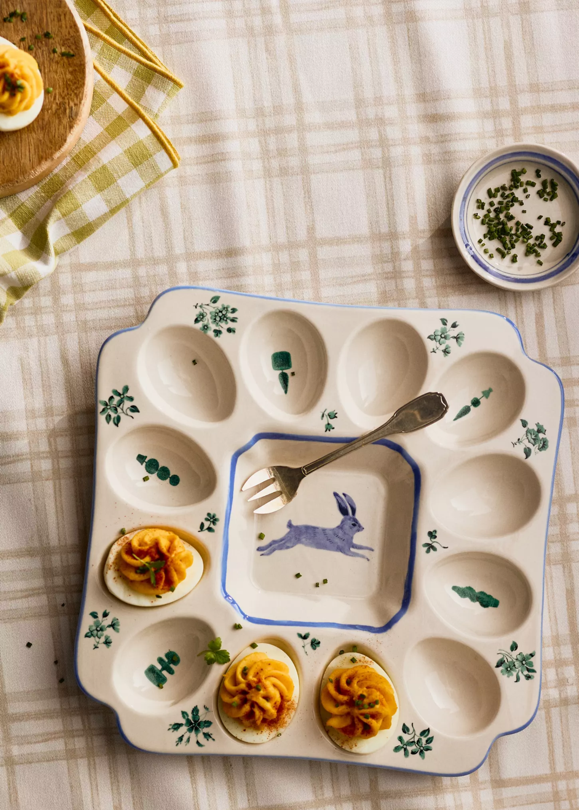 A table with a devilled egg platter beside a bowl of chopped chives