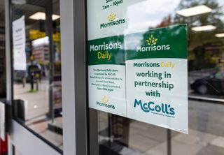 A sign in a shop window reading 'Morrisons Daily working in partnership with McColl's'