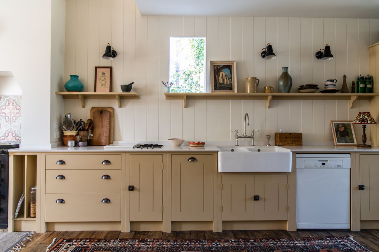 Cream painted kitchen with sink and dishwasher and open shelving on paneled wall