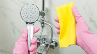 gloved hands showing how to clean a shower head with a microfibre cloth