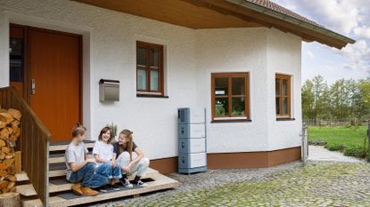 Three children sitting outside a family home with BLUETTI energy storage devices.