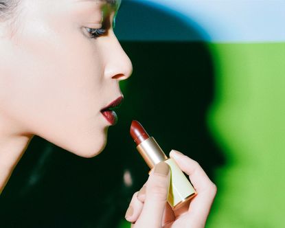 Woman putting on red Dries Van Noten lipstick, illustrating our beauty products round-up