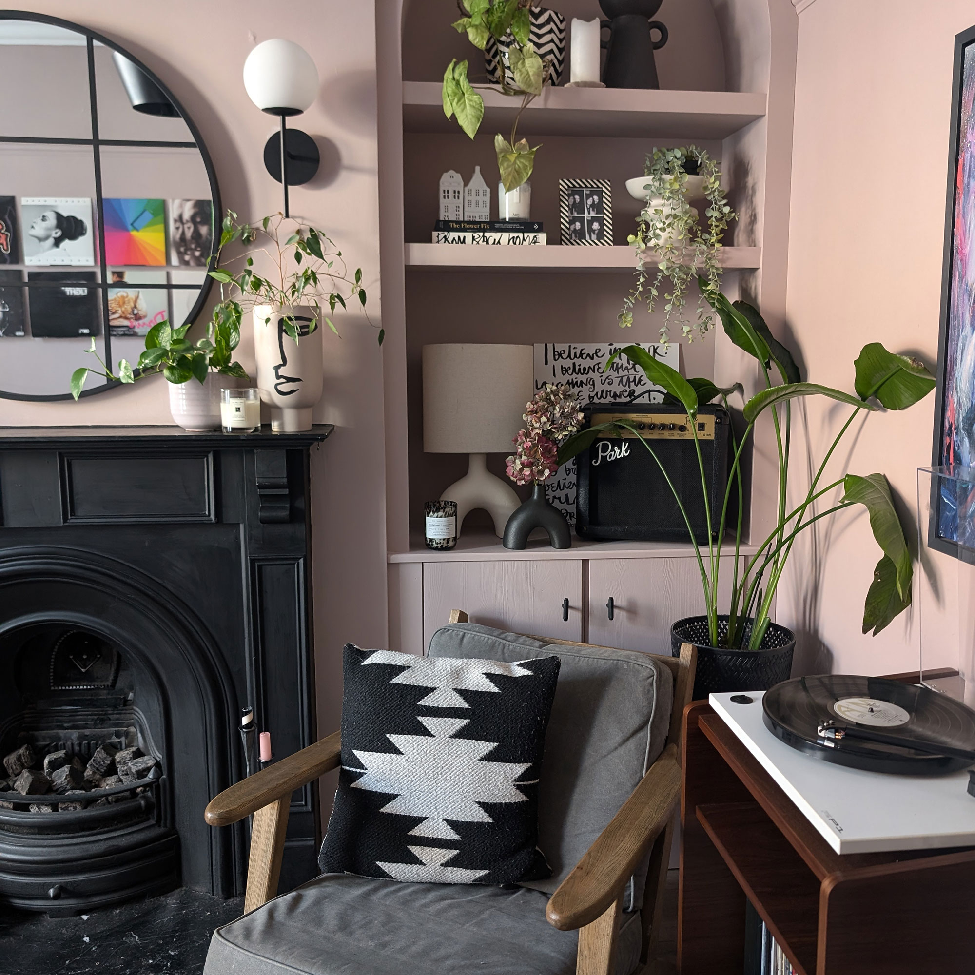 Corner of dusky pink living room with in-built shelving, mid-century armchair, vinyl player and black fireplace