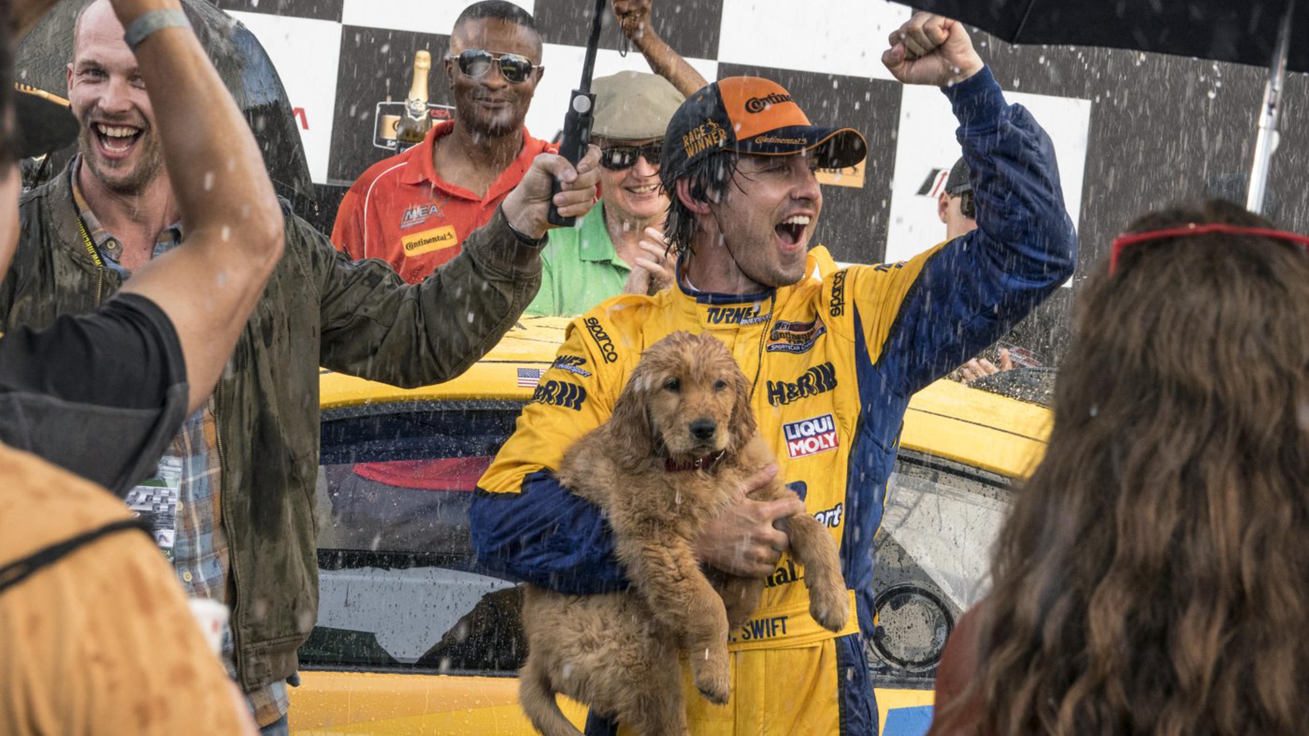 A man standing celebrating his racing car win while holding a puppy in his arms