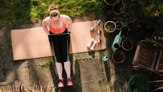 Woman stretching with resistance band in back garden on a yoga mat in the sunshine