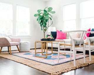 Bright and breezy boho living room with layered rugs, large plant in corner, curved coffee table, and pink color pop cushions on sofa.