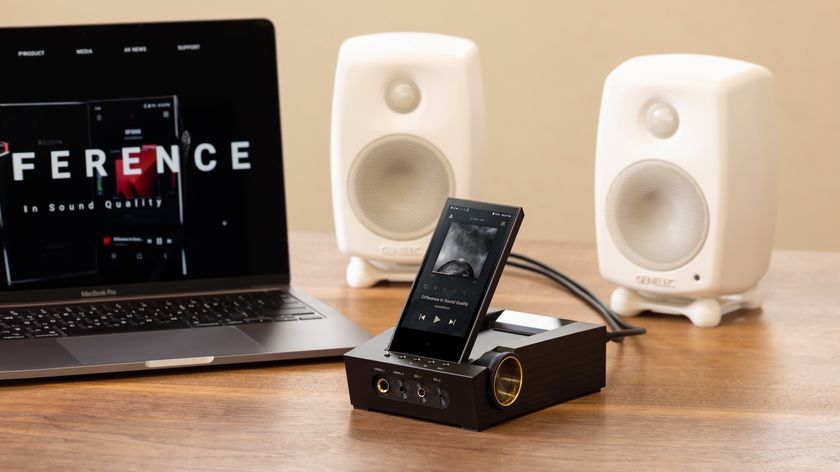 The Astell&amp;Kern CA1000T on a wooden surface in front of a laptop and speakers.