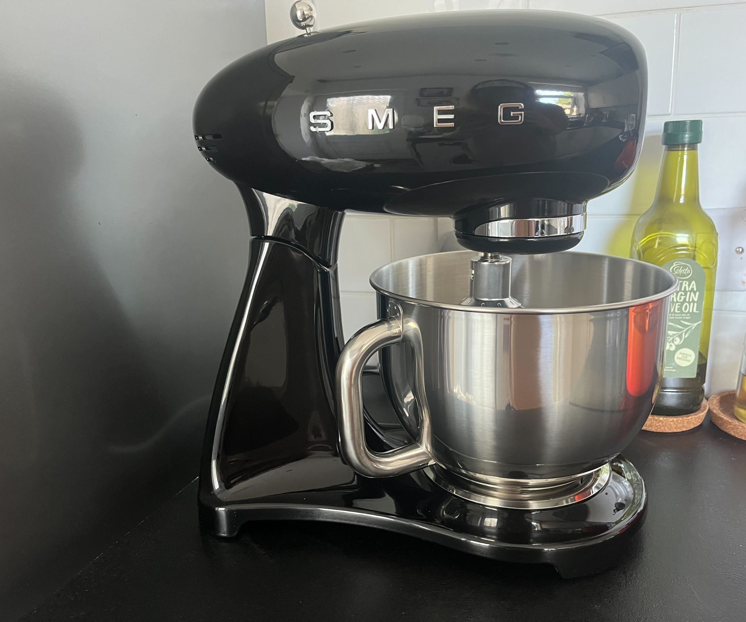 A black SMEG brand stand mixer on a kitchen counter.
