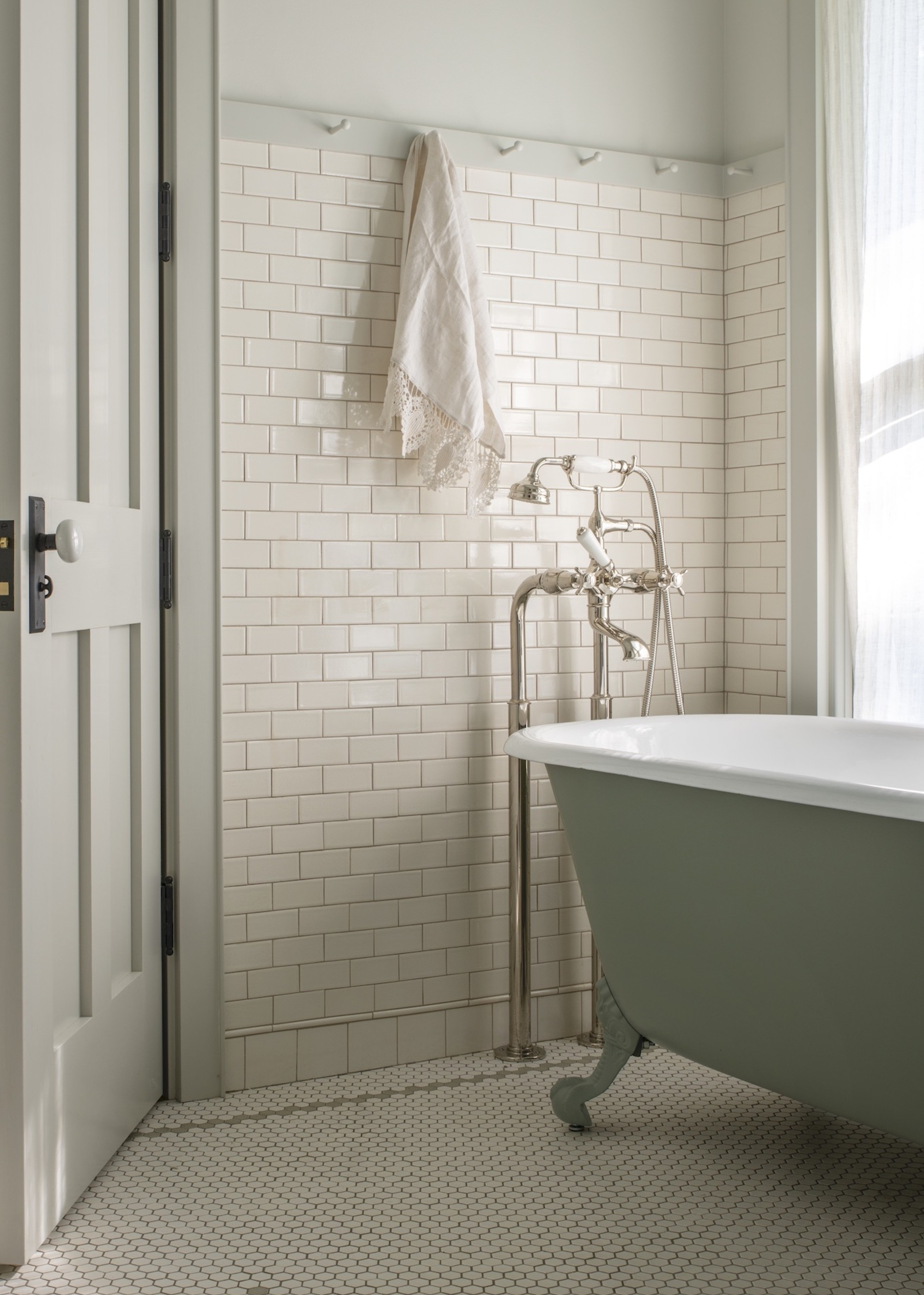 A bathroom with a mosaic tile floor, a green freestanding bathtub, and white subway tiled walls
