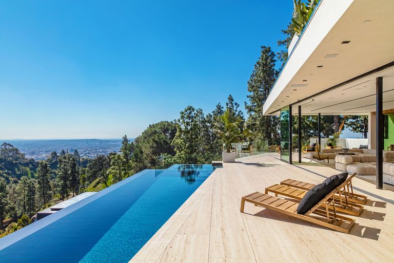 How much does it cost to build a pool, illustrated by a hilltop infinity pool with wooded views outside a modern glass house designed by Richard Landry.