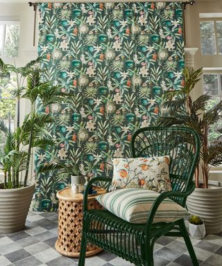 Green chair in orangery with printed curtain behind, and rattan side tables and plants