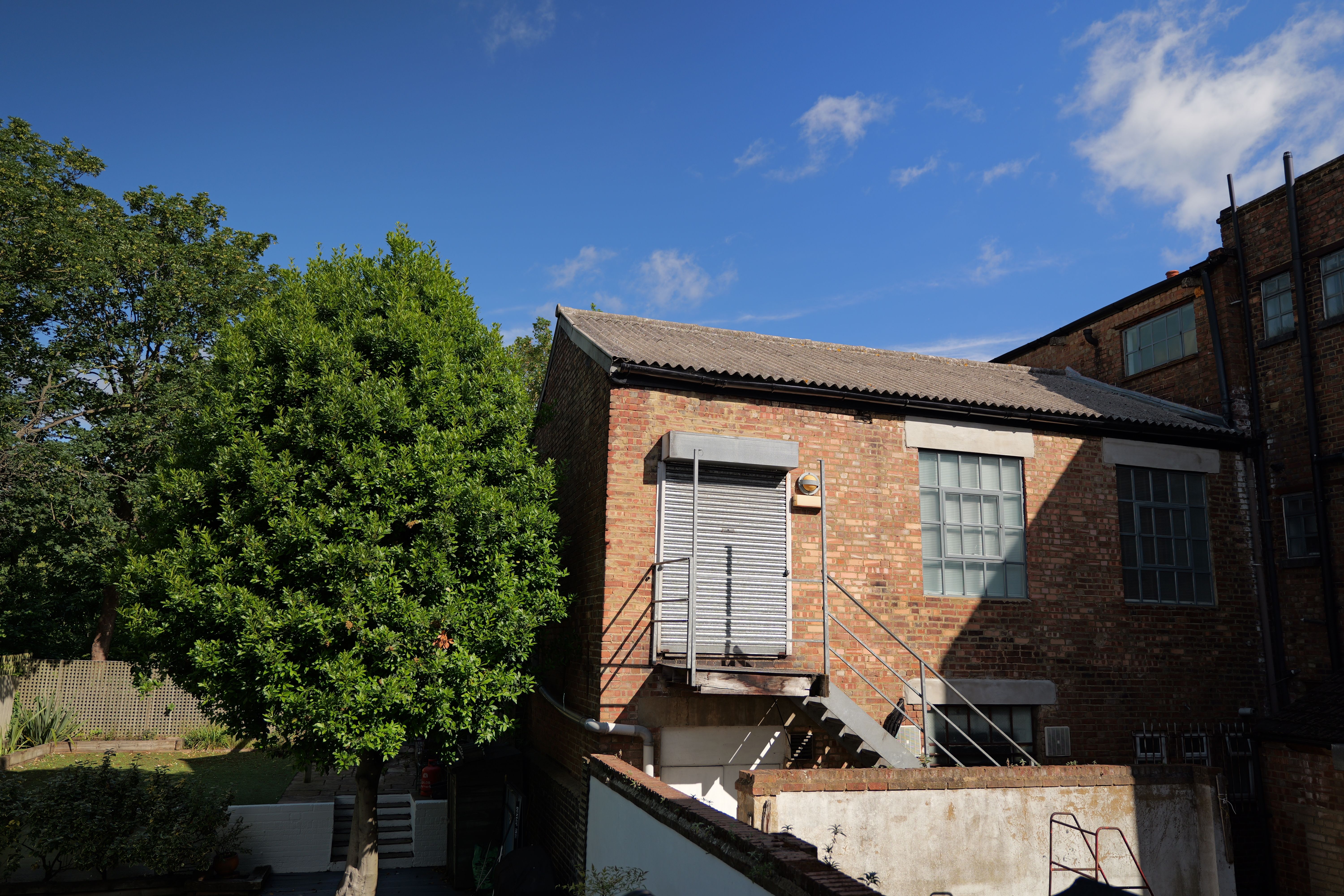 A warehouse next to a tree in front of a bright blue sky